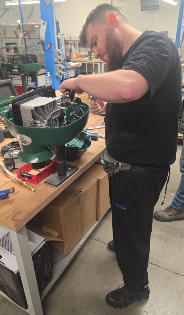 Piège Mosquito Magnet démonté sur un établi d'atelier, capot ouvert et composants apparents, en cours de réparation par un technicien IJN+