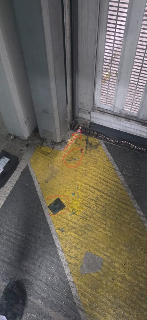 Bas de la porte du parking souterrain d'une copropriété de Gennevilliers, avec la broche métallique du poste d'appâtage et un reste de sachet traînés au sol, entourés en rouge