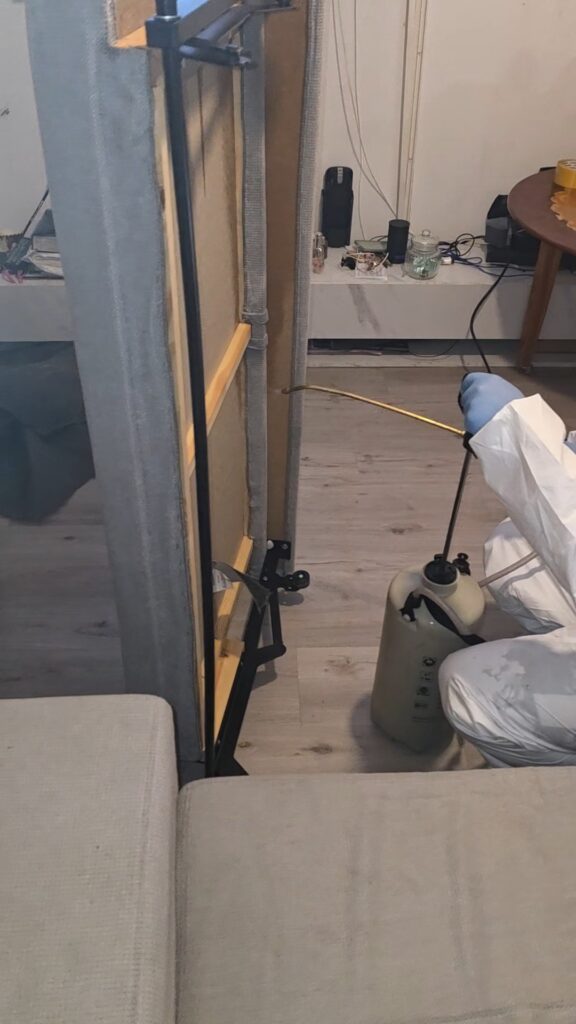 Technicien IJN+ en combinaison blanche et gants traitant à la lance le montant métallique d'un lit, lors d'une intervention punaises de lit à Ecquevilly